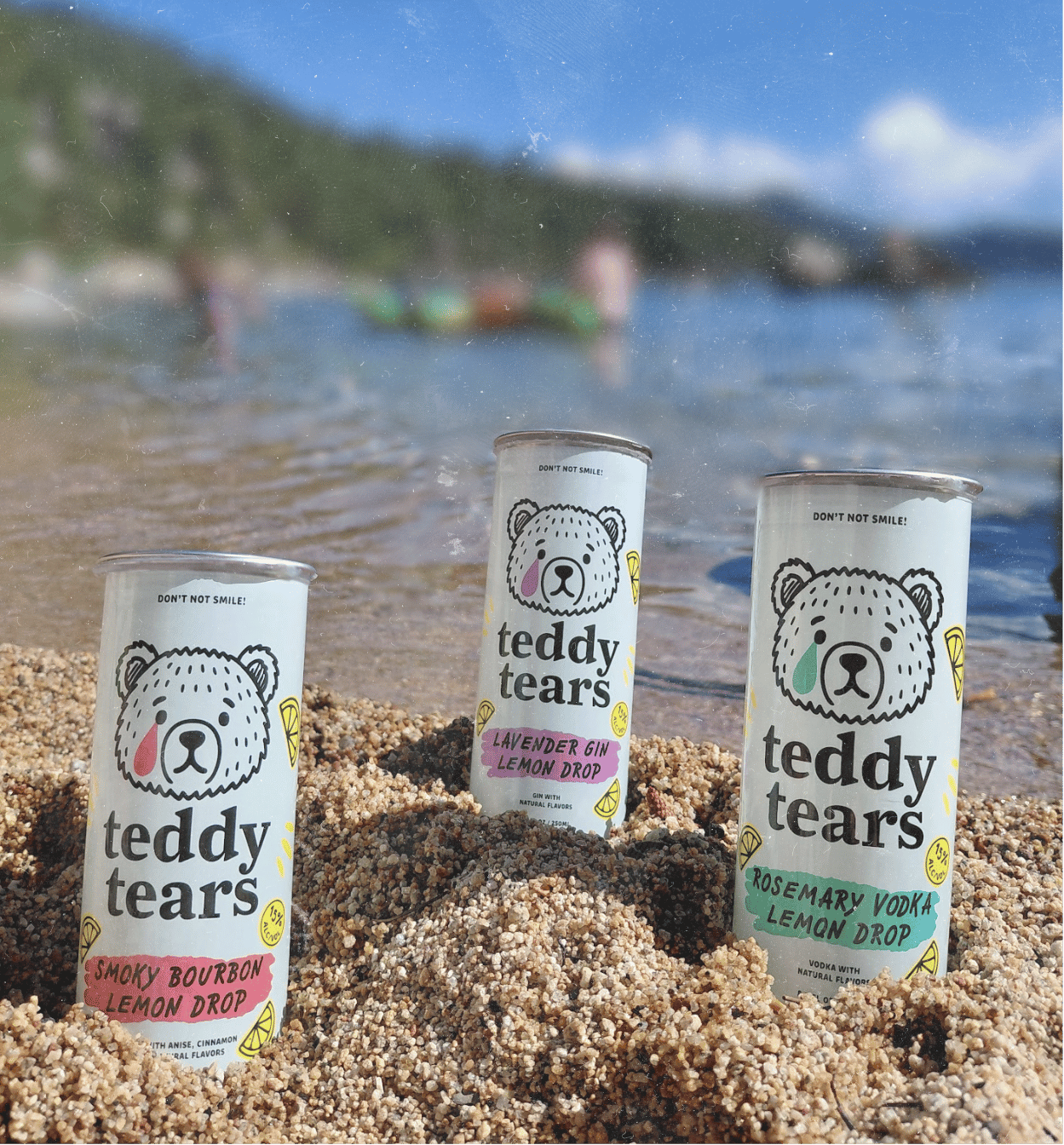 Teddy Tears cans on beach with mountain lake background
